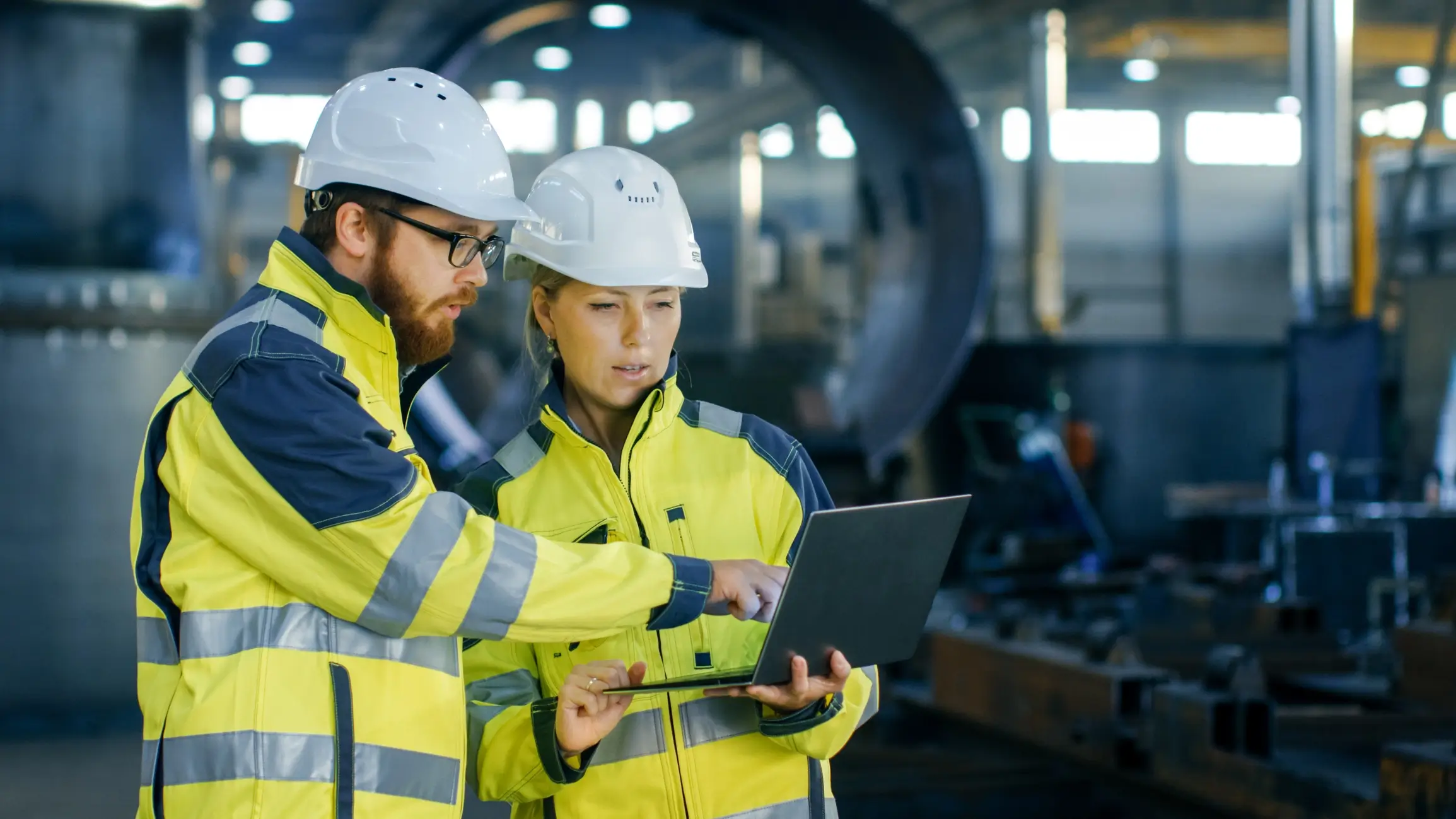 Industrial engineers reviewing a digital assessment on a laptop inside a factory